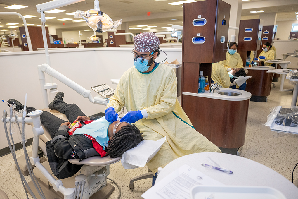 A male dental hygiene student cleans a little boy's teeth.