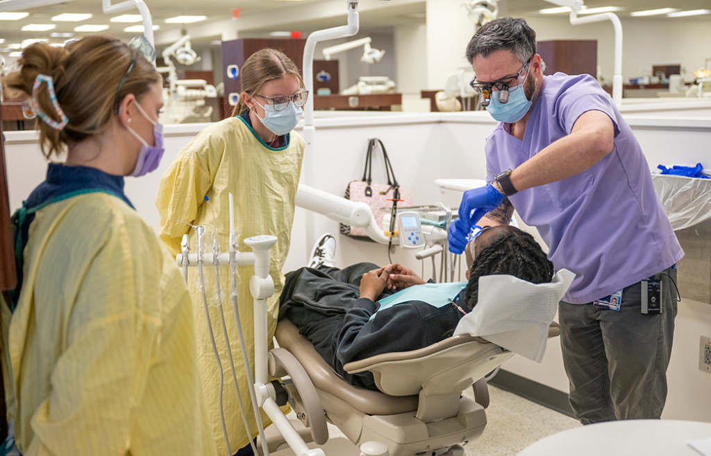 Two female dental hygiene students observe as a male dental hygienist cleans a little boy's teeth.