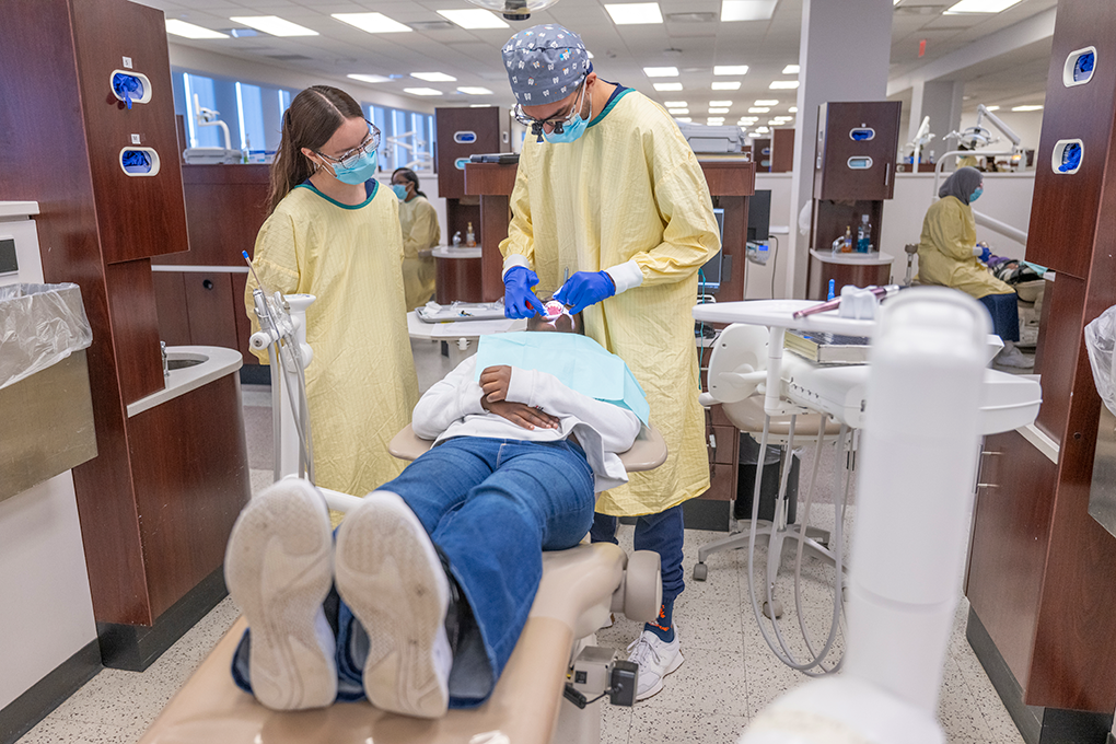 A female and a male dental hygiene student clean a young girl's teeth.