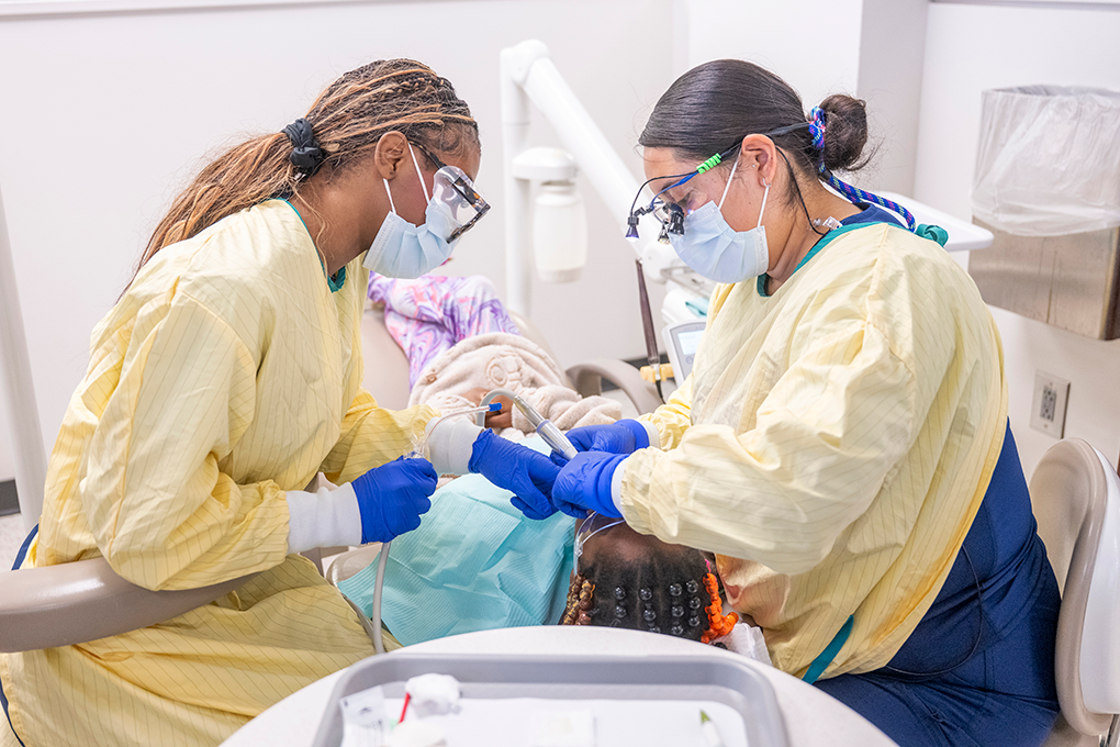 Two dental hygiene students clean a little girl's teeth.