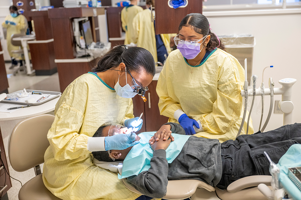 Two female dental hygiene students clean a little boy's teeth.