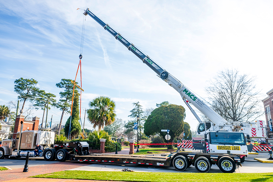 A crane lifts a large tree up in the air on the campus of a university.