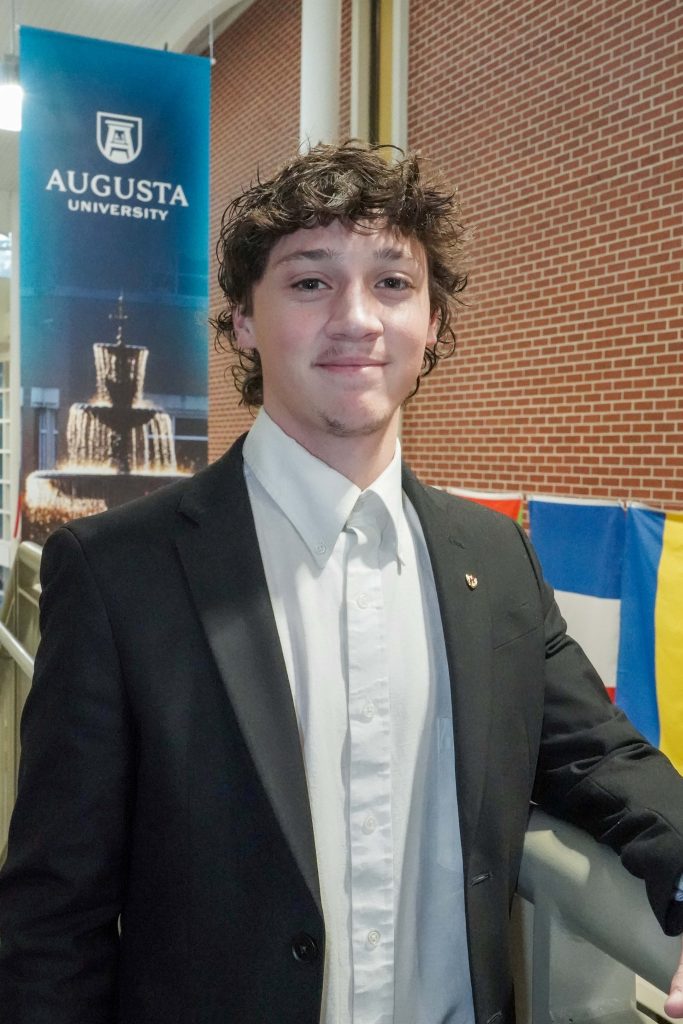 With an arm propped on a stairwell, a guy smiles for a photo.