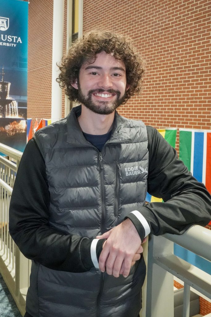 With an arm propped on a stairwell, a guy smiles for a photo.