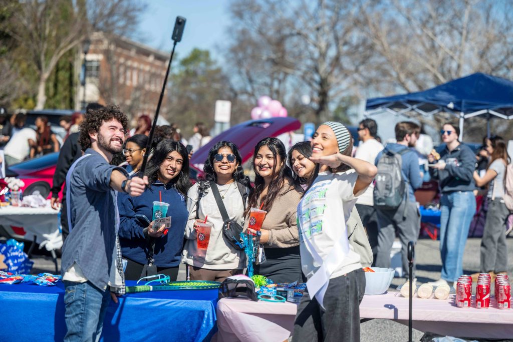 A man holding a selfie stick takes a photo of himself and a group of women.