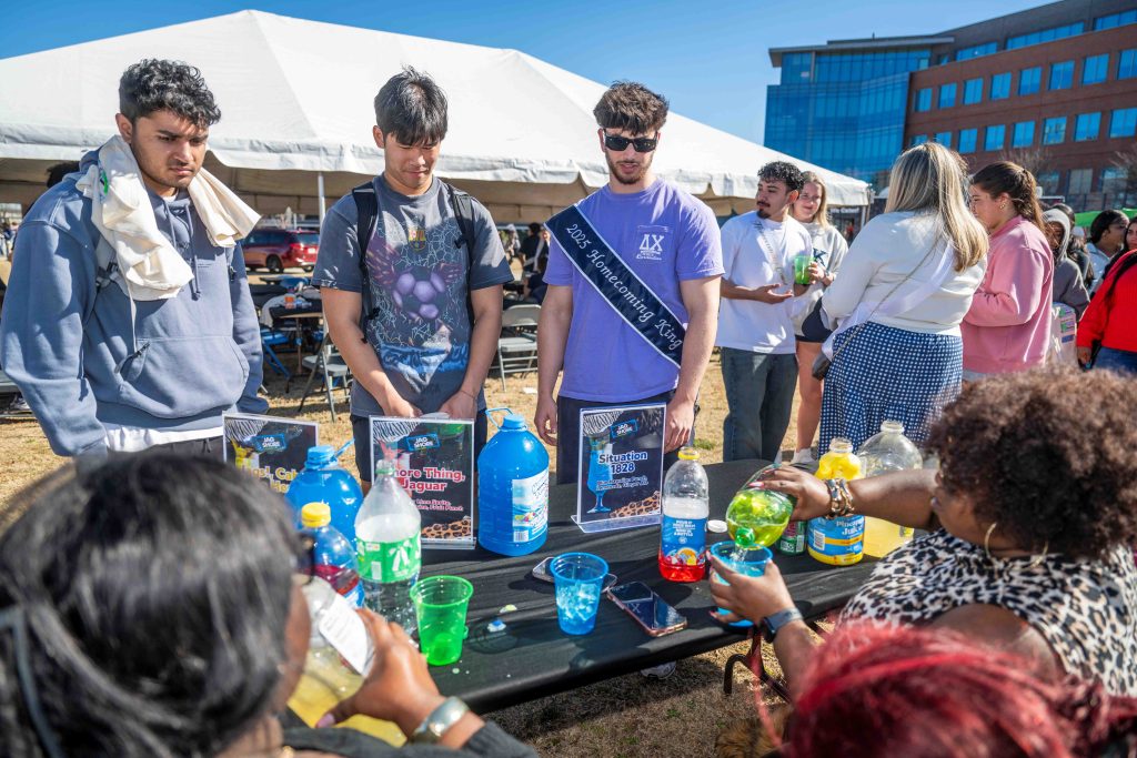 A group of men stand in front of a table as a woman pours juice into a cup.