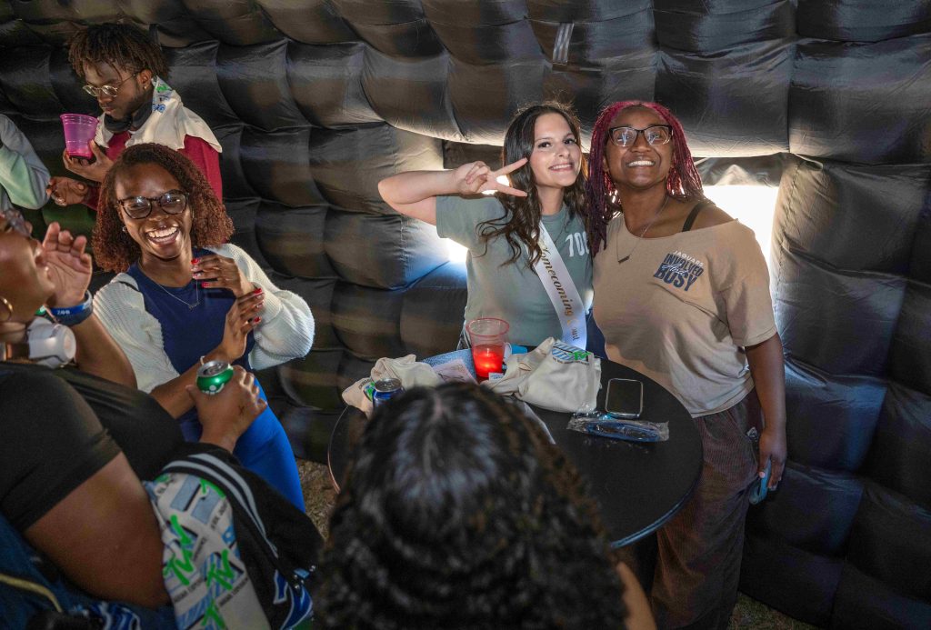 A group of college-aged students stand smiling and laughing inside an inflatable house.