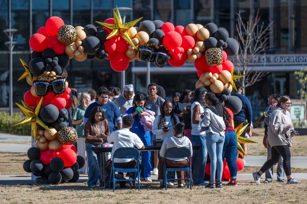 Students gather in front of a table set beneath a colorful balloon arch.