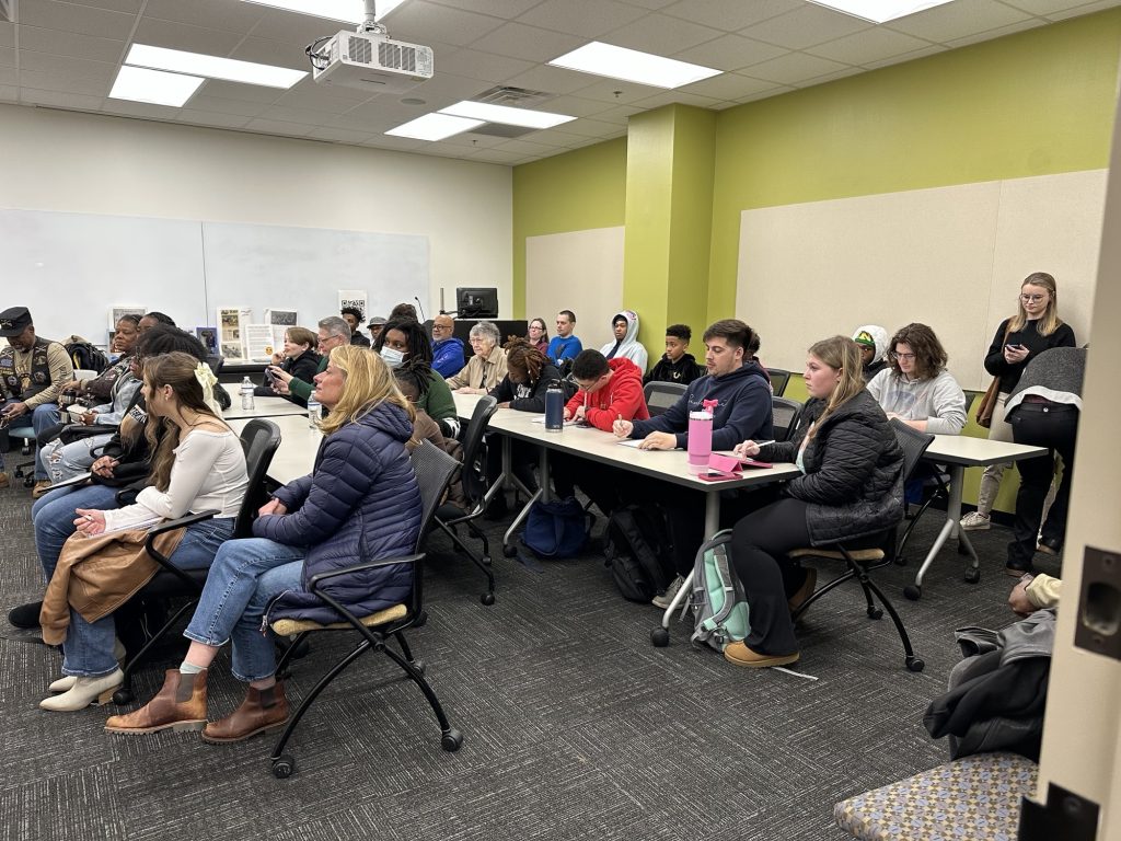 A group of students sit at tables inside a classroom.