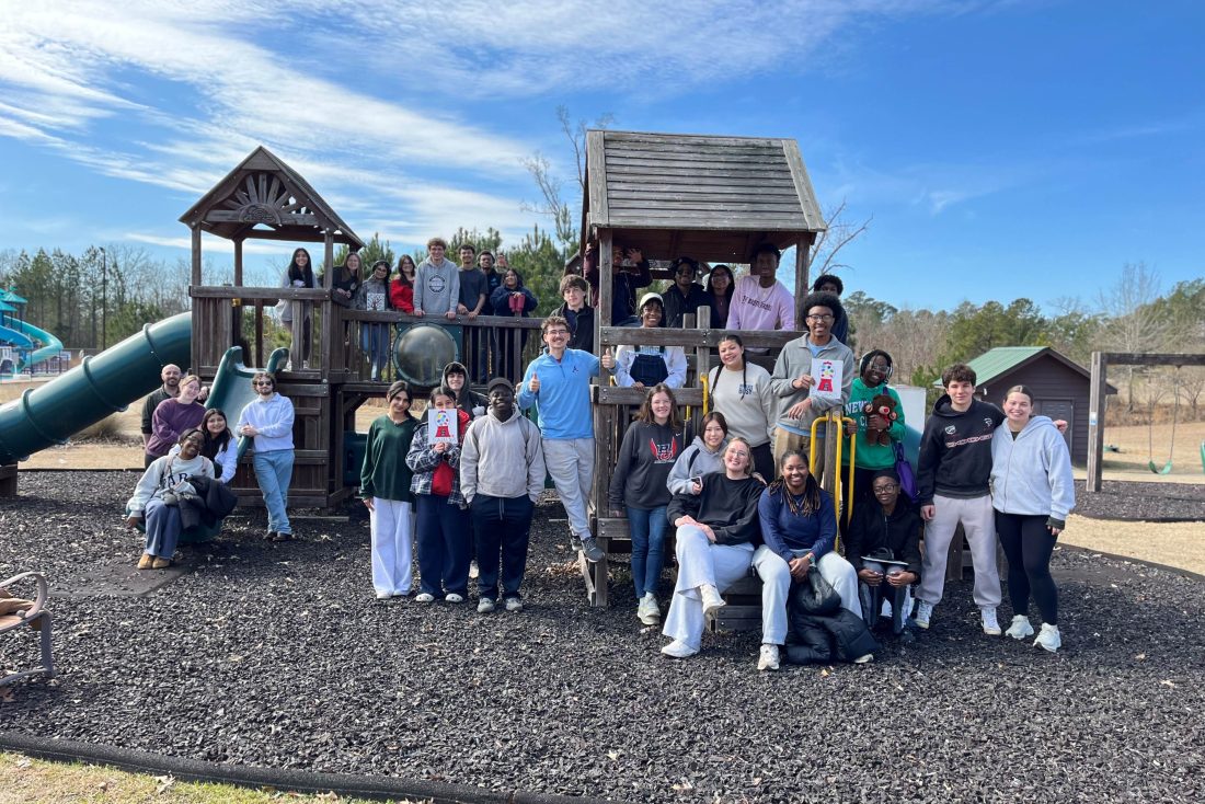 A large group and men and women on a children's playground pose for a photo.