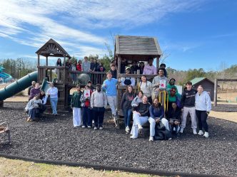 A large group and men and women on a children's playground pose for a photo.