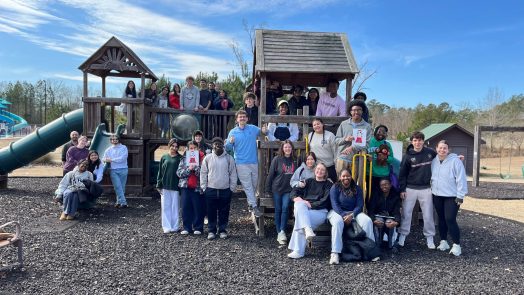 A large group and men and women on a children's playground pose for a photo.