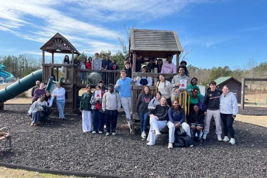 A large group and men and women on a children's playground pose for a photo.
