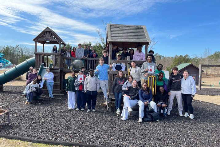 A large group and men and women on a children's playground pose for a photo.