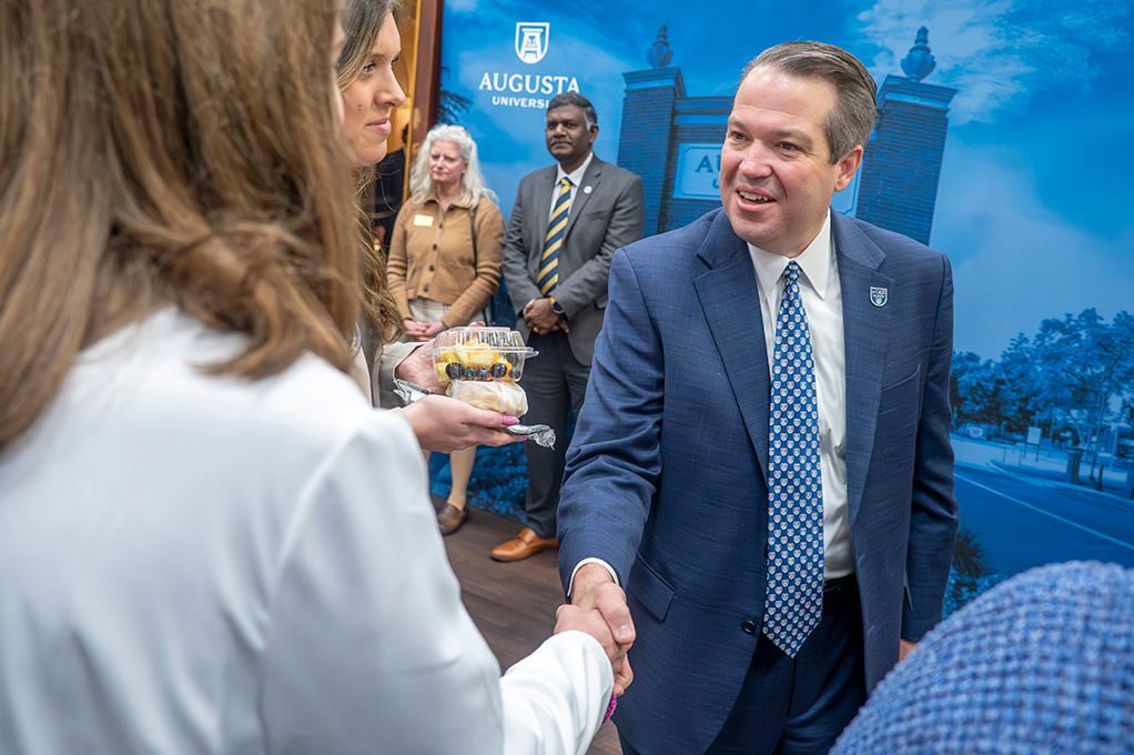 A man in business dress shakes the hand of a woman wearing a white doctor's coat.