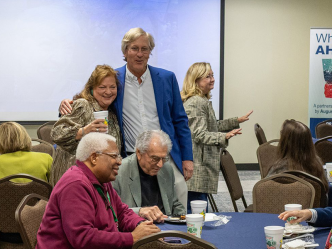 A man and a woman share a friendly side hug during an event celebrating the woman's retirement.