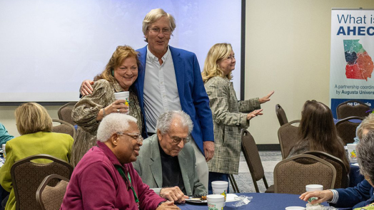 A man and a woman share a friendly side hug during an event celebrating the woman's retirement.