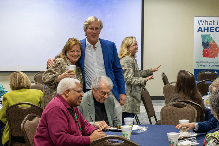 A man and a woman share a friendly side hug during an event celebrating the woman's retirement.