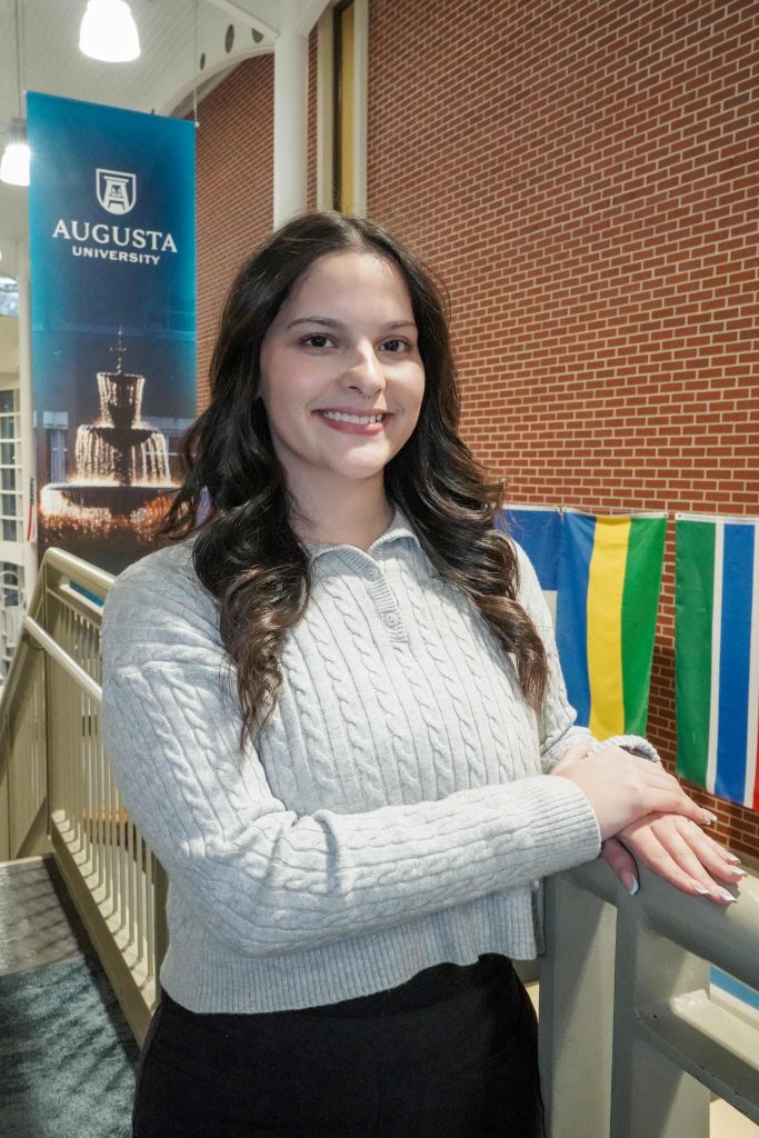 With an arm propped on a stairwell, a girl smiles for a photo.