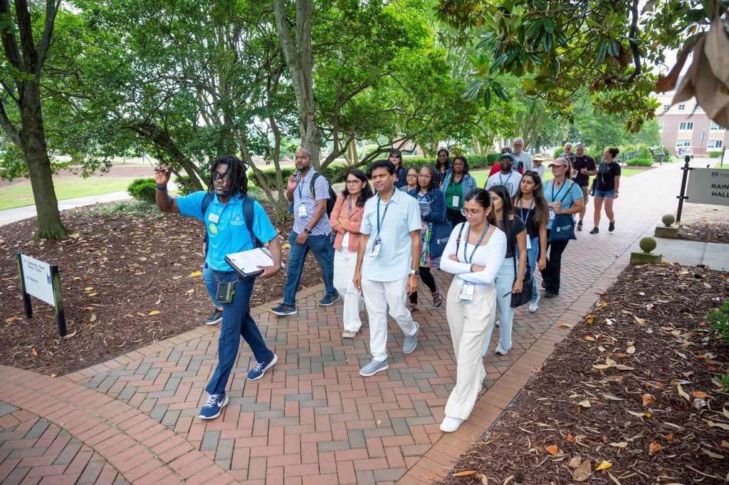 A group of men and women walking down a brick path with a canopy of trees overhead.
