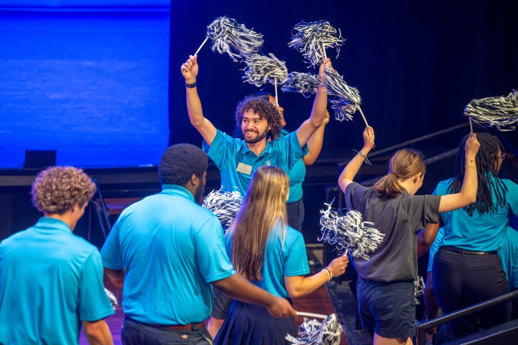 Men and women hold pom poms walk in a single file line.