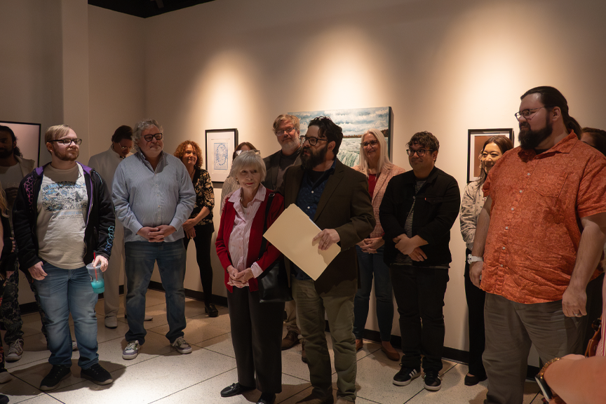 Woman and man stand together in a gallery full of people.