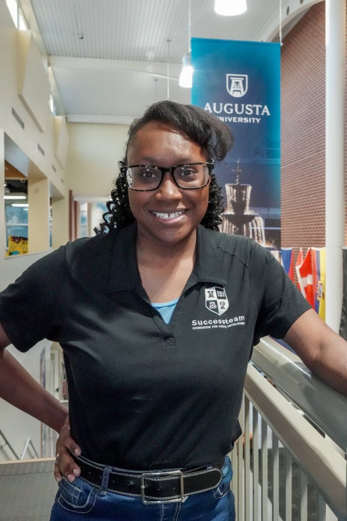 With an arm propped on a stairwell, a girl smiles for a photo.