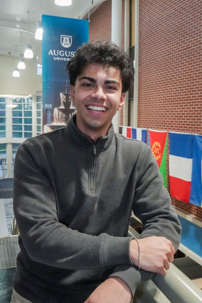 With an arm propped on a stairwell, a guy smiles for a photo.