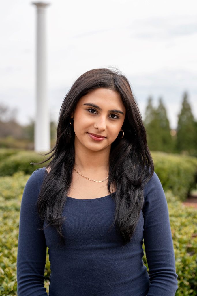 A smiling woman with greenery in the background.