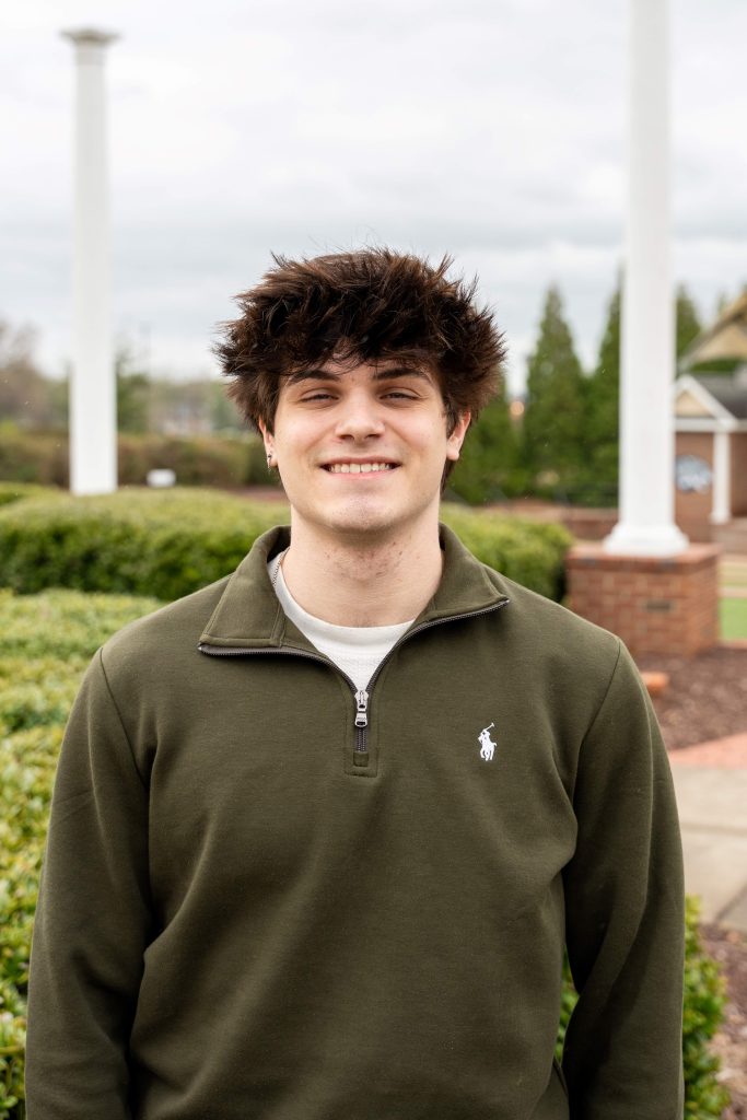 A smiling man with greenery in the background.