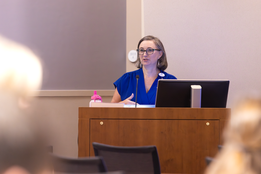 A woman presents to a large crowd of medical students and doctors in a large classroom.