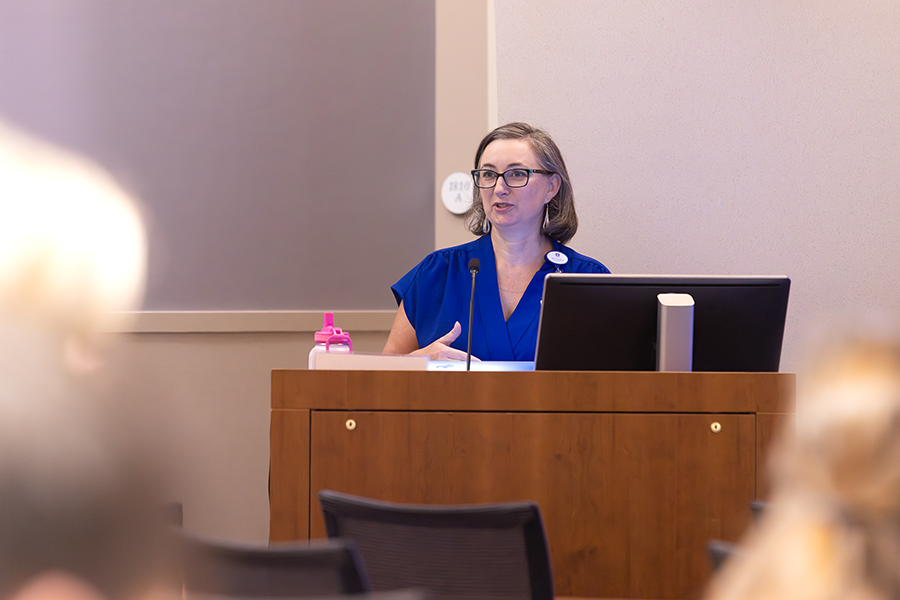 A woman presents to a large crowd of medical students and doctors in a large classroom.