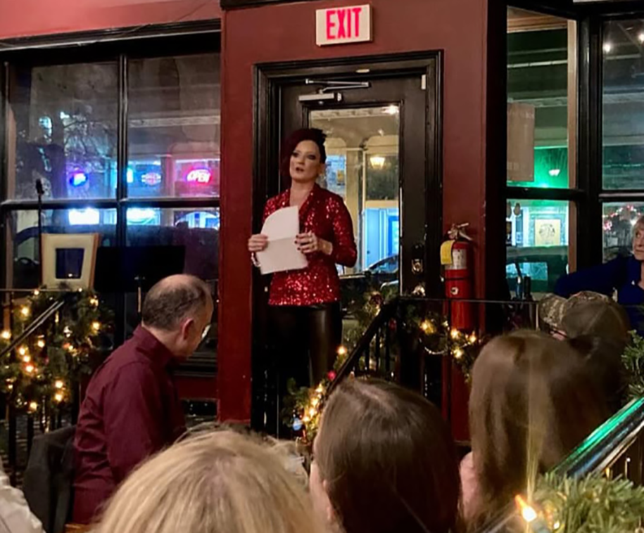 A woman standing in front of a group of people in a room and speaking to them around Christmas time.