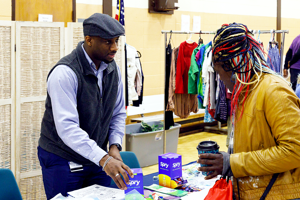 A man stands behind a table set up with dental hygiene products while a woman looks at the table.