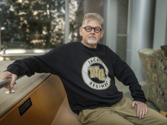 A man sitting on a bench with his right arm sitting on a railing.