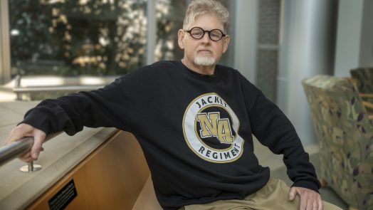 A man sitting on a bench with his right arm sitting on a railing.
