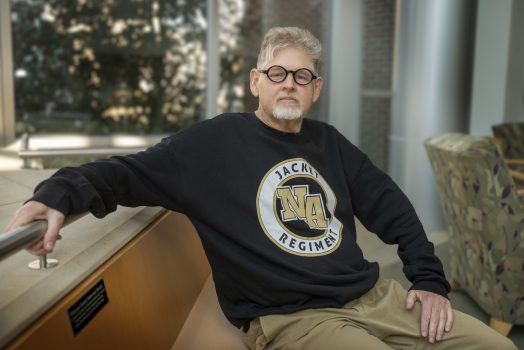 A man sitting on a bench with his right arm sitting on a railing.