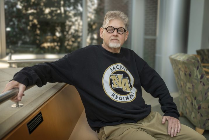 A man sitting on a bench with his right arm sitting on a railing.