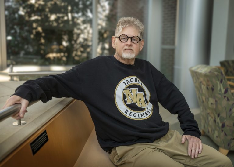 A man sitting on a bench with his right arm sitting on a railing.