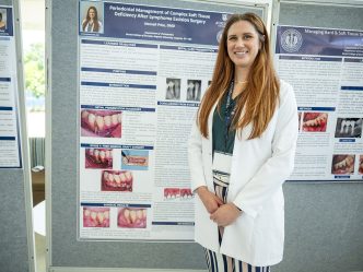 A female dental resident smiles in front of a poster of her research.