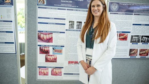 A female dental resident smiles in front of a poster of her research.