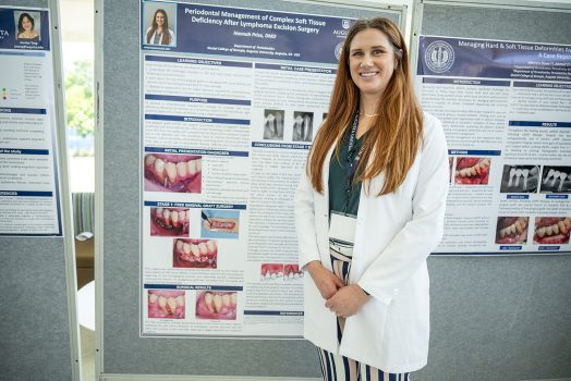 A female dental resident smiles in front of a poster of her research.