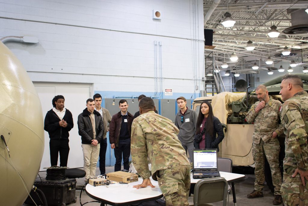 Students standing around table and equipment listening to instructor.