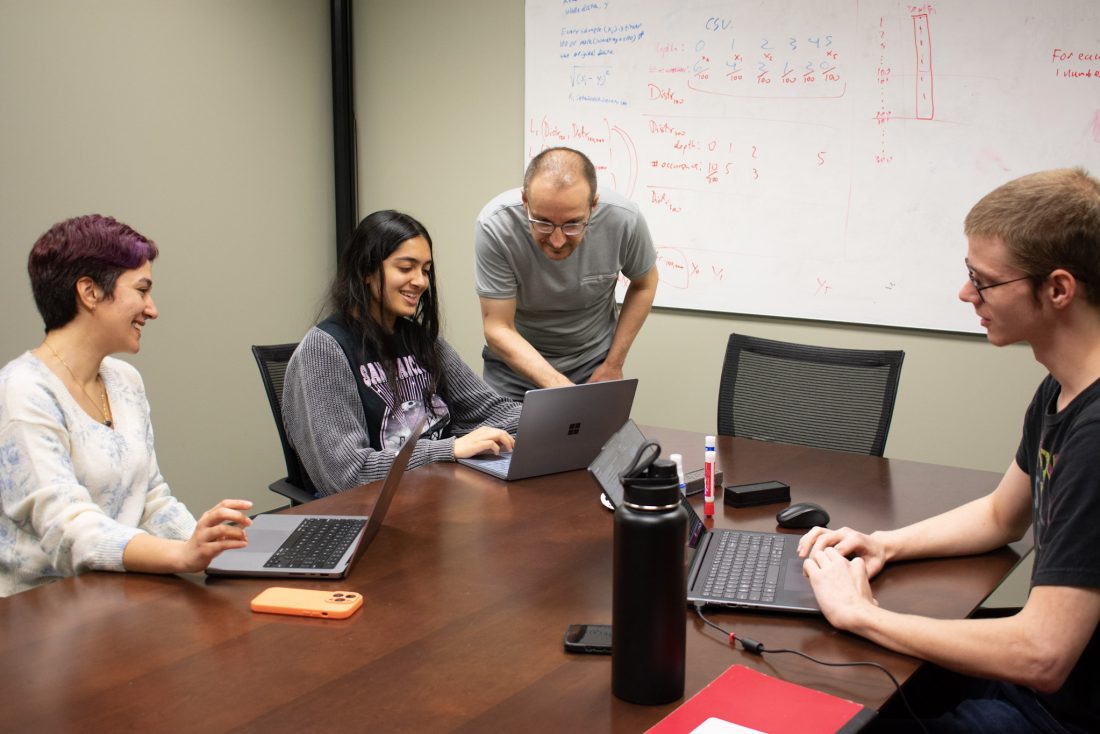 Professor interacting with students while their on their laptops in classroom.