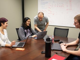 Professor interacting with students while their on their laptops in classroom.