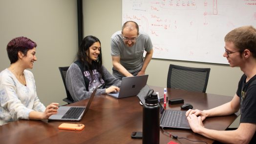 Professor interacting with students while their on their laptops in classroom.