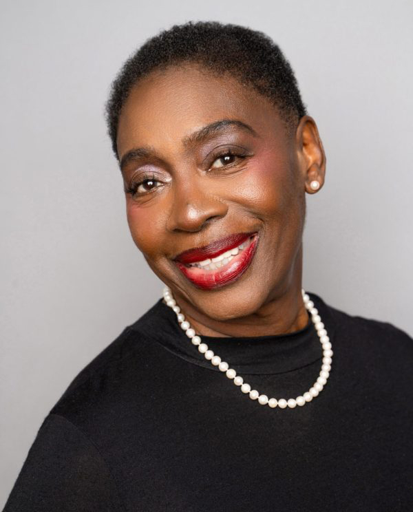 Professional headshot of a woman in a black shirt and pearls, her hair is short