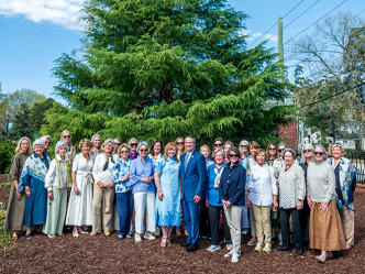 Large group of ladies and one man in front of a large tree.