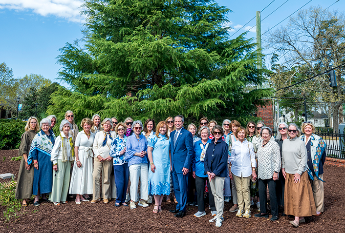 Large group of ladies and one man in front of a large tree.