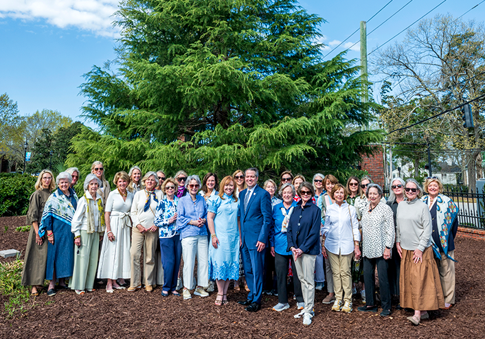 Large group of ladies and one man in front of a large tree.